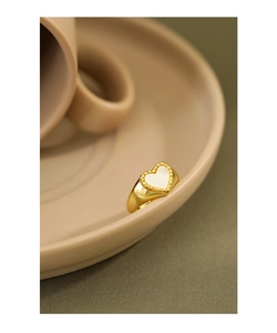 Macro detail of a heart-shaped shell ring in gold plating on a minimalist ceramic plate