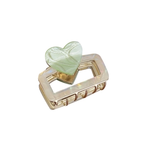 Pinza per capelli in metallo dorato con cuore decorativo e dettaglio perlato su fondo bianco