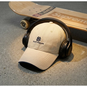 Detail view of beige cotton baseball cap with blue embroidery and headset on skateboard
