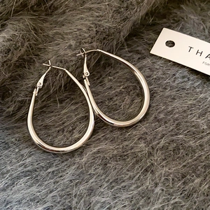 Detail of minimalist silver oval hoop earrings resting on a soft grey plush background