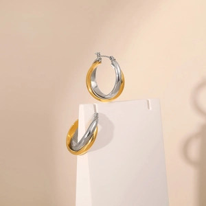 Polished two-tone gold and silver crossover hoop earrings on a geometric display stand