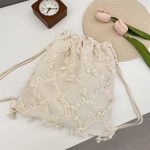 Detail of cream tassel canvas backpack with textured fringe grid and woven drawstring cord