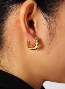Close-up of minimalist gold-plated square hoop earring worn on a woman's earlobe