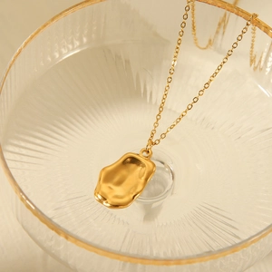 Golden pendant necklace displayed inside a luxury gold-rimmed glass for artistic detail