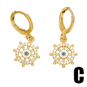 Golden evil eye earrings with rudder pendant and cross elements on a white background
