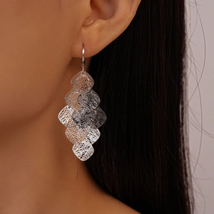 Close-up of geometric hollow mesh rhombus fringe earrings worn by a model in silver