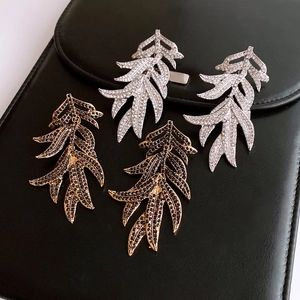 Macro shot of gold and silver leaf earrings with rhinestones on black leather background
