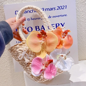 Detail of woven straw handbag featuring vibrant faux orchids and pearl bow decoration
