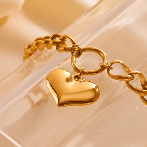Polished gold heart pendant on a chunky curb chain bracelet shown on a soft beige background