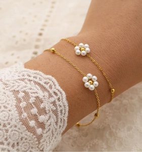 Close-up of double-layer gold chain bracelet with white pearl daisy charms on lace