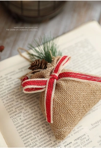 Detail of burlap Christmas gift bag with red plaid ribbon and pine cone on a book