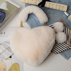 Close-up of heart-shaped faux fur bag with plush pom-poms and golden chain strap