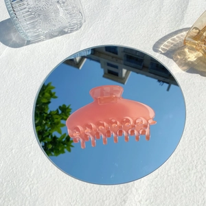 Artistic shot of a matte pink shark hair claw clip reflecting clear sky on a round mirror