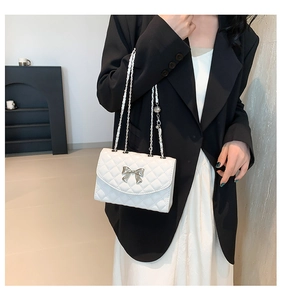 Detail of white quilted crossbody bag with silver bow accent and chain strap