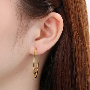 Close-up of golden C-shaped stainless steel earrings with colorful zircon stones on model