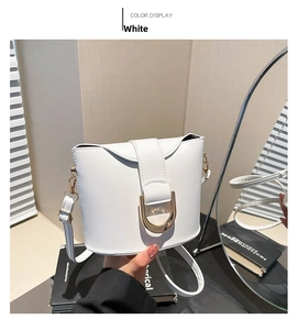 Detail view of a white bucket bag with gold U-shaped buckle and adjustable shoulder strap