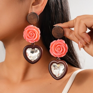 Détail de boucles d'oreilles bohèmes avec fleur en résine rose et pendentif cœur en bois