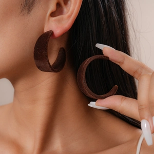 Detailed close-up of brown flocked C-shaped earrings with soft velvet texture on ear