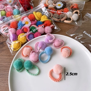 Detail of 2.5cm colorful plush ball hair ties in a daisy print bag on wood surface