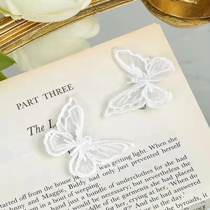 Pair of delicate white embroidered lace butterfly hair clips on an open vintage book page