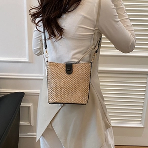 Beige woven straw bucket bag with dark strap, perfect for summer beach holidays