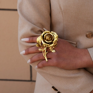 Close-up of a large gold metallic rose flower ring with detailed petals on model's hand