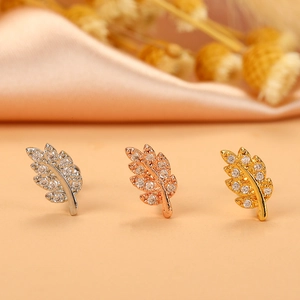 Macro detail of three leaf-shaped stud earrings in silver, gold, and rose gold with zircons
