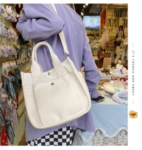 Detailed close-up of white canvas tote featuring front pocket with metal snap button