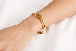 Close-up of a gold clover bracelet with chunky chain on a white textured background