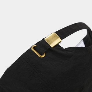 Détail de la sangle réglable en tissu noir et boucle en métal doré mat sur une casquette