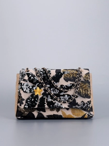 Macro shot of detailed floral embroidery with black and gold sequins on a beige woven bag