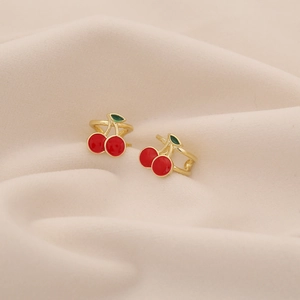 Close-up of cherry ear clips with red enamel fruit and green leaves on beige velvet