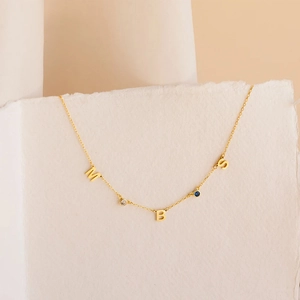 Detalle de un collar dorado con colgantes de letras MBS y piedras de nacimiento