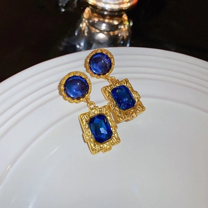 Detailed macro view of vintage gold earrings with blue stones and pearls on white tray