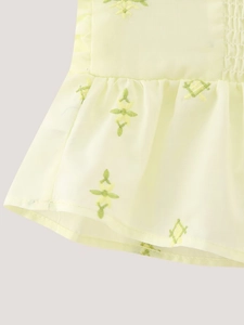 Gros plan sur tissu jaune avec broderie florale verte et détails de bord volanté