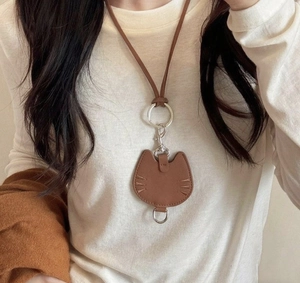 Detailed view of a brown leather cat-shaped pendant with strap on a white sweater