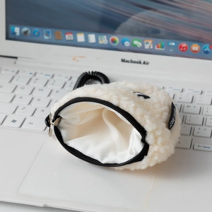 Macro detail of white sherpa fleece coin purse with black zipper on laptop keyboard