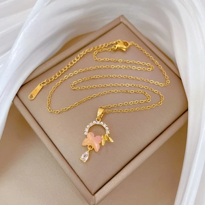 Detailed view of titanium gold necklace with pink butterfly, pearls and drop-shaped gem