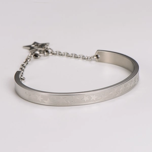 Detalle de brazalete de acero inoxidable plateado con relieve de estrella y colgante