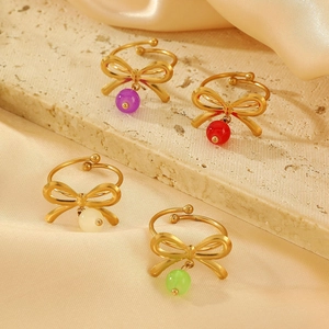 Detailed view of gold bow rings with colorful bead charms on elegant silk and stone backdrop
