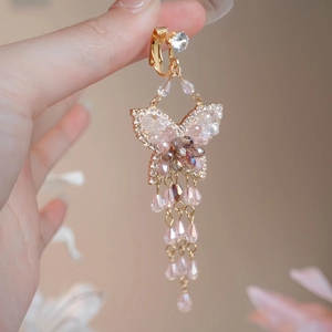 Détail macro de boucles d'oreilles papillon dorées avec cristaux roses et glands