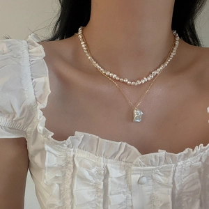 Detail of double-layer necklace with baroque pearls and gold chain on white blouse