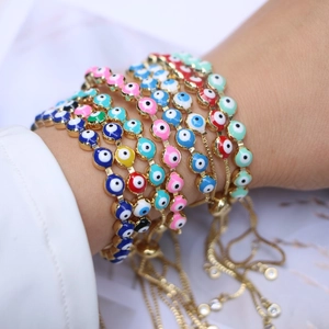 Close-up of stacked evil eye bracelets with colorful enamel charms and golden chains