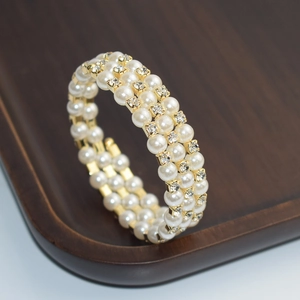 Close-up of a three-layer pearl and rhinestone bracelet with golden finish on wood