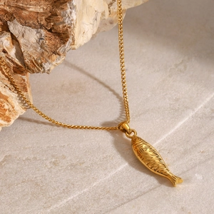 Detailed view of a gold fish pendant necklace with textured scales on stone background