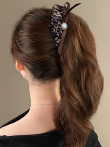 Detail of leopard print bow hair clip with pearls shown on a high ponytail style