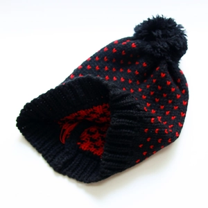 Detail der Strickmütze mit schwarz-roten Herzmustern und großem flauschigem Bommel