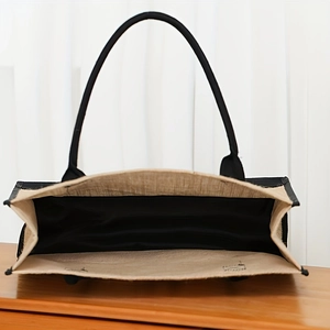 Eco-friendly jute tote bag with black handles and spacious interior on wooden background
