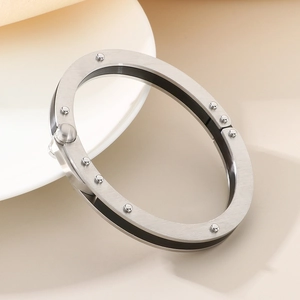 Detail of brushed silver stainless steel bangle with decorative rivets on a white plate