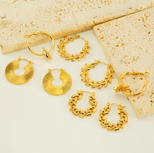 Detailed close-up of various gold-plated star and textured hoop earrings on stone